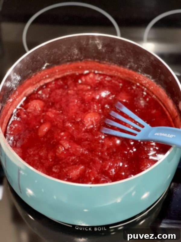 Rich, red strawberry syrup in a pot on the stove, after sugar has been added and thickened to perfection.