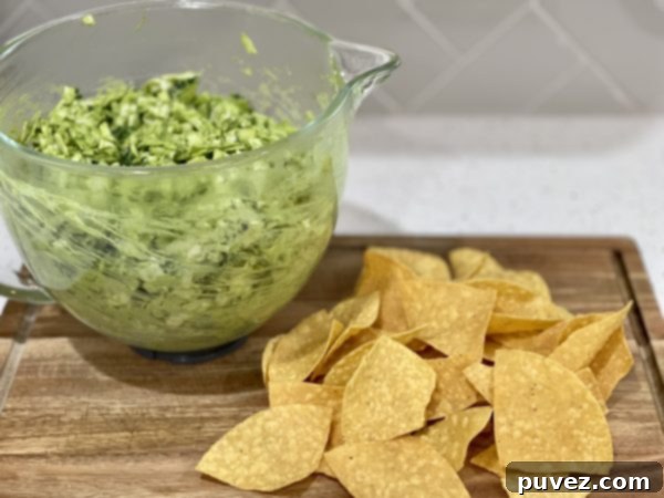 A vibrant Green Goddess Salad in a clear glass bowl, artfully arranged on a rustic wooden cutting board, with a side of crispy tortilla chips, inviting a healthy and delicious meal.