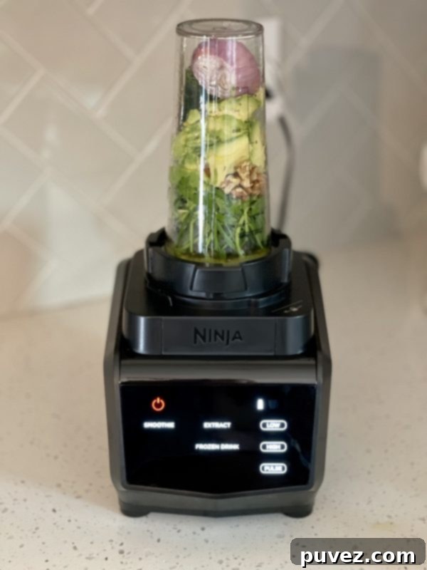 A high-speed blender filled with a lush, vibrant green mixture, actively blending the ingredients for the creamy and flavorful Green Goddess dressing.