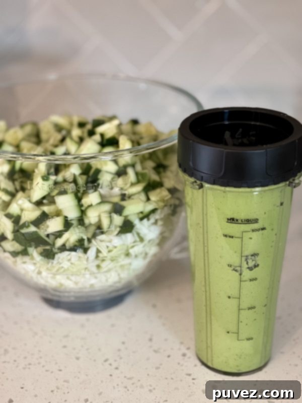 The vibrantly dressed Green Goddess Salad in a glass bowl, perfectly mixed and ready to serve, positioned next to the blender containing the remaining creamy dressing.