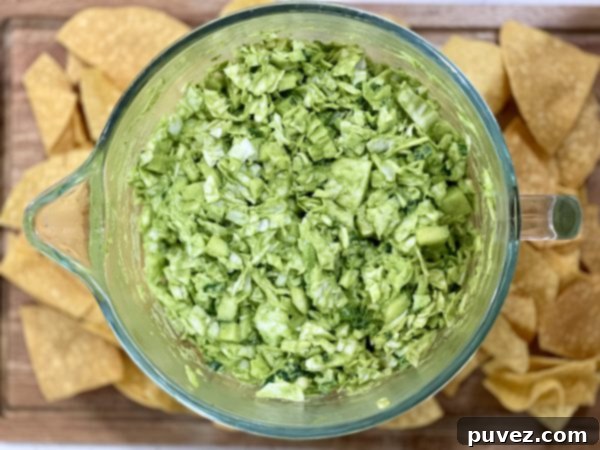 The Green Goddess Salad, perfectly dressed and vibrant, presented in a clear glass bowl on a wooden cutting board, accompanied by a handful of crispy chips, inviting a delightful snacking experience.