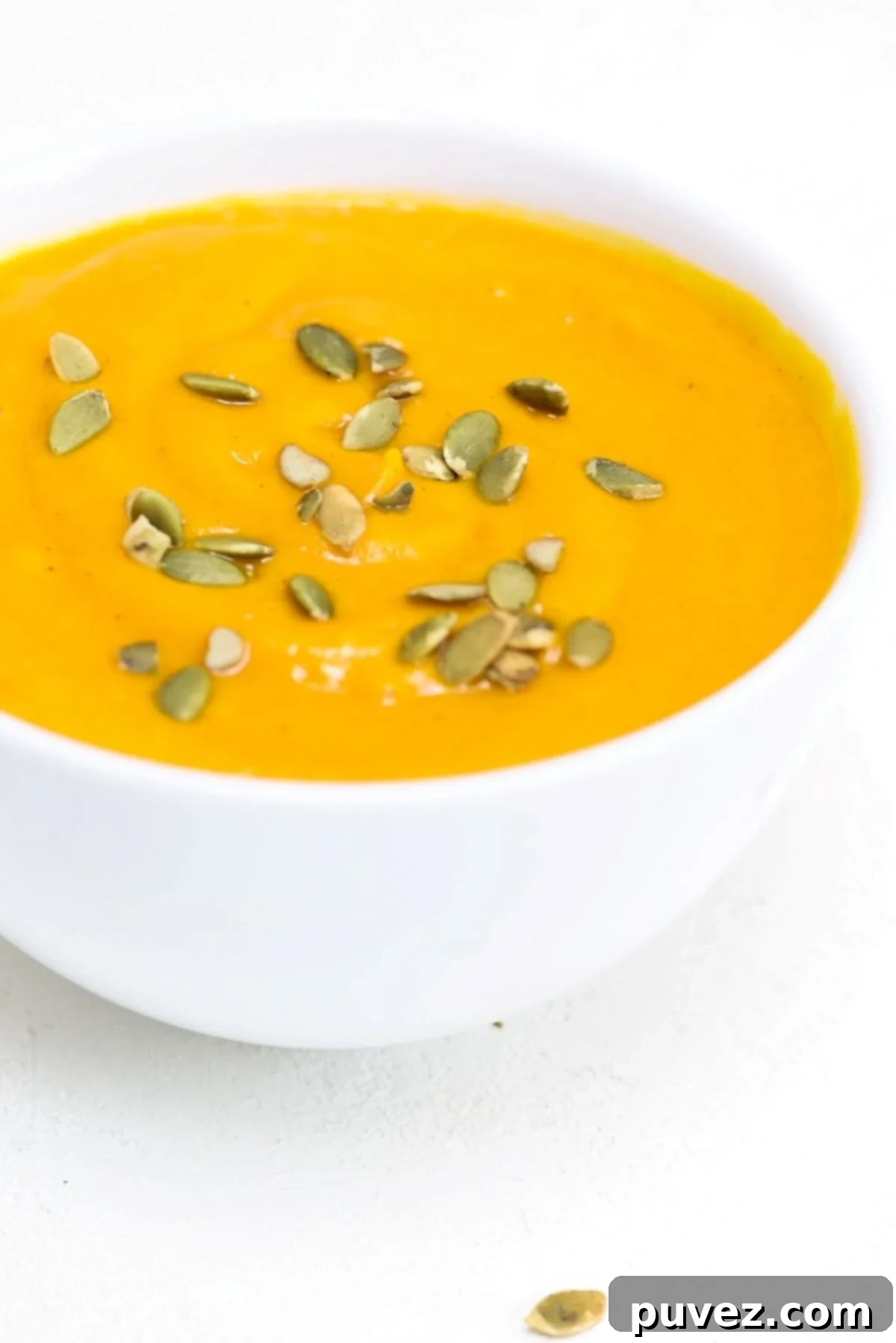 Carrot Butternut Squash Soup in a white bowl and topped with pumpkin seeds.