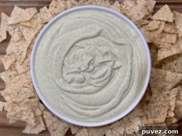 Creamy Jalapeno Dip in a bowl with tortilla chips surrounding it on a wood cutting board