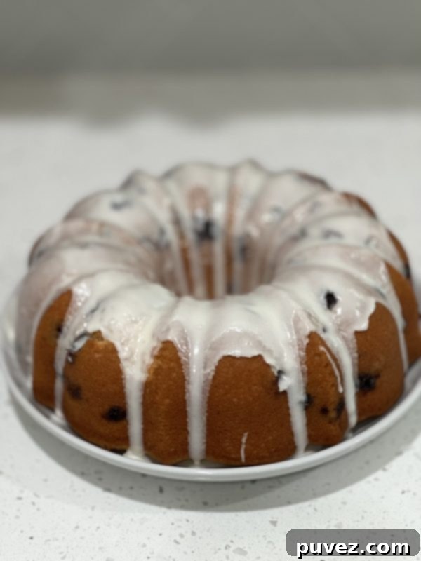 A fully glazed Lemon Blueberry Pound Cake on a serving plate, glistening with lemon glaze.