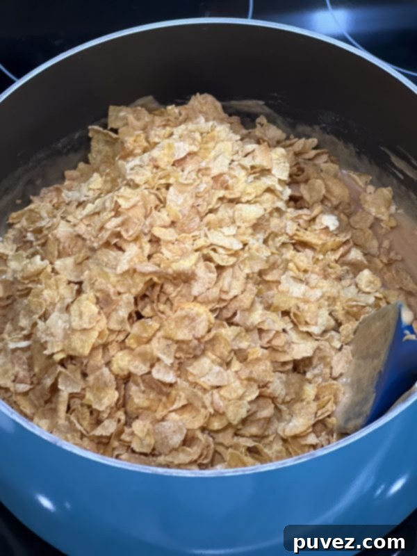 Corn flakes being added to the rich peanut butter mixture in a large saucepan