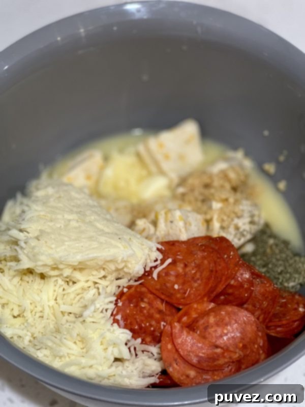 Ingredients in a mixing bowl: chopped biscuits, pepperoni, mozzarella, garlic, Italian seasoning, and melted butter