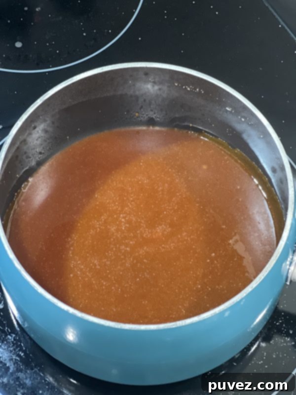 Silky Smooth Salted Caramel Sauce bubbling gently in a saucepan, showing its rich, golden-brown color and smooth consistency after combining all ingredients.