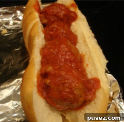Numerous round Italian meatballs gently simmering in a bubbling, rich red tomato sauce in a large pot.