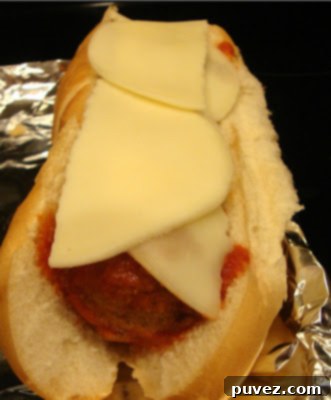 A freshly prepared meatball sub in a toasted roll, filled with meatballs and sauce, before cheese is added.