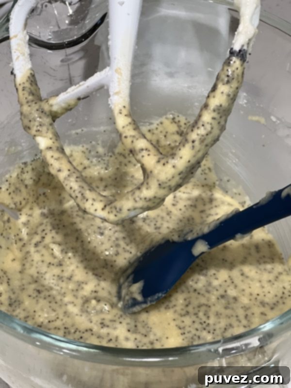 Close-up of lemon poppy seed cupcake batter in a stand mixer bowl, showing the creamy texture and poppy seeds.