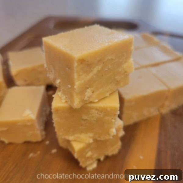 Several squares of creamy peanut butter fudge stacked on a rustic cutting board, highlighting its appealing texture.