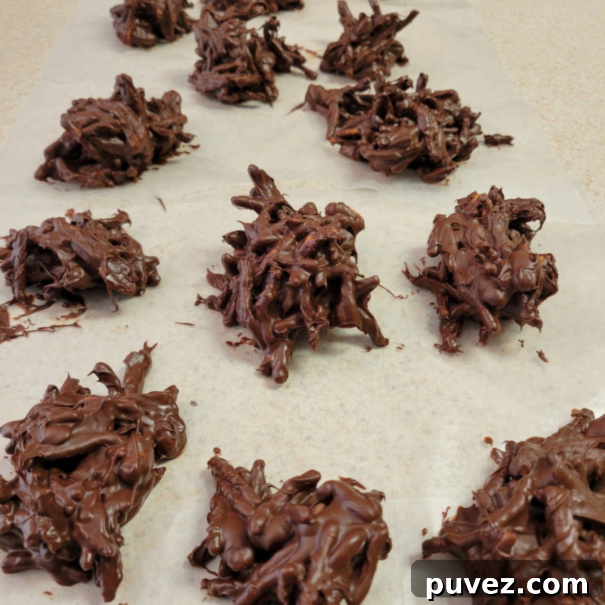 Wax paper covered with numerous chocolate haystacks in various stages of drying and cooling, showcasing a freshly made batch.