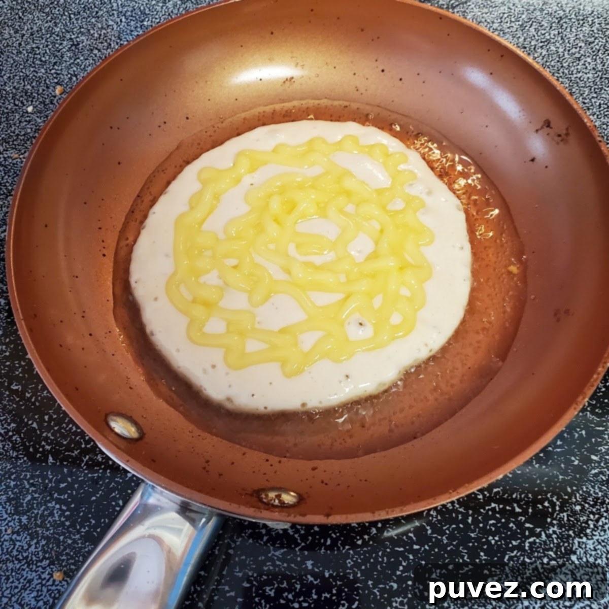 A single banana pudding pancake cooking on a griddle, showing the pudding and wafer topping before flipping