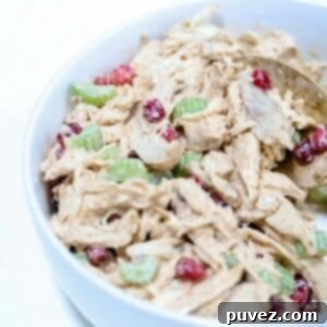 Up close picture of chicken pomegranate salad in a white bowl with a gold serving spoon.