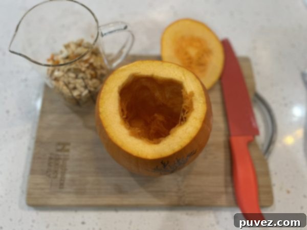 a pumpkin with the top cut off and the seeds and guts taken out and put into a glass measuring cup sitting on a wooden cutting board.
