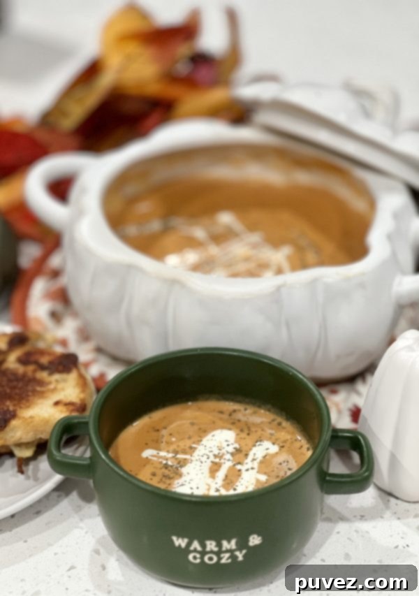 Creamy Pumpkin Soup in a green soup bowl in front of a pumpkin-shaped serving bowl holding the rest of the soup