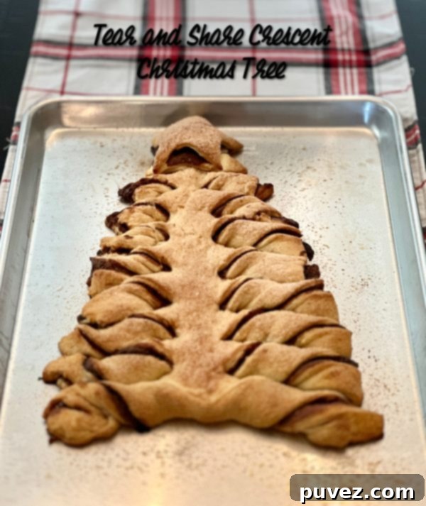 A beautifully baked Tear & Share Crescent Christmas Tree, golden brown and glistening with cinnamon sugar, resting on a cookie sheet over a festive plaid table runner, ready to be enjoyed.