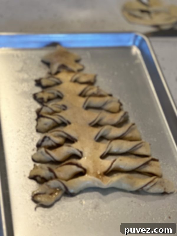 Unbaked Tear & Share Crescent Christmas Tree, brushed with butter and sprinkled with cinnamon sugar, sitting on a baking sheet, ready for the oven.