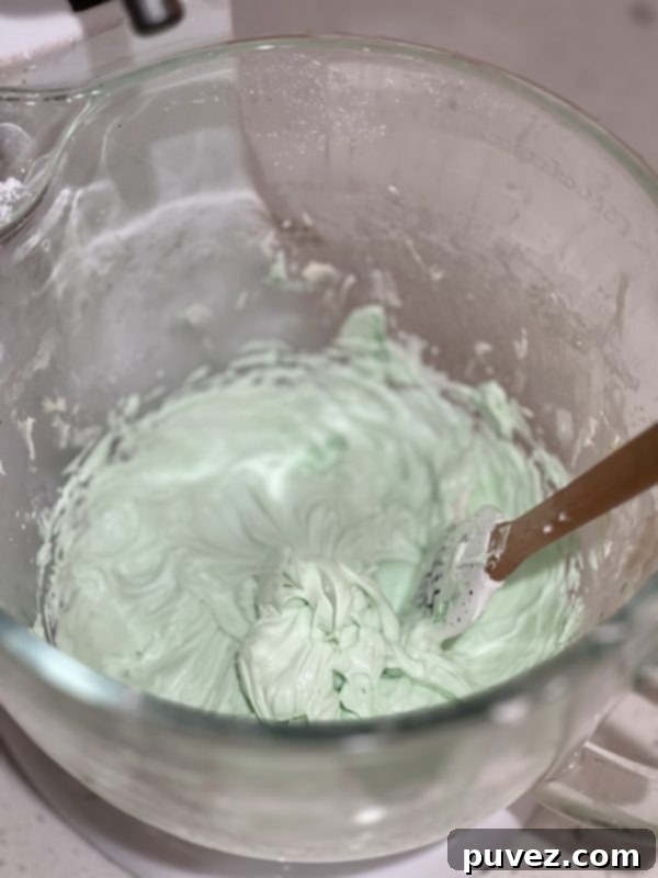 Vibrant green Grasshopper Pie Cookie Cups frosting in a clear glass mixing bowl, looking perfectly smooth and fluffy.