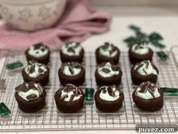 Finished Grasshopper Pie Cookie Cups arranged neatly on a metal cooling rack, topped with green frosting and chopped Andes mints.