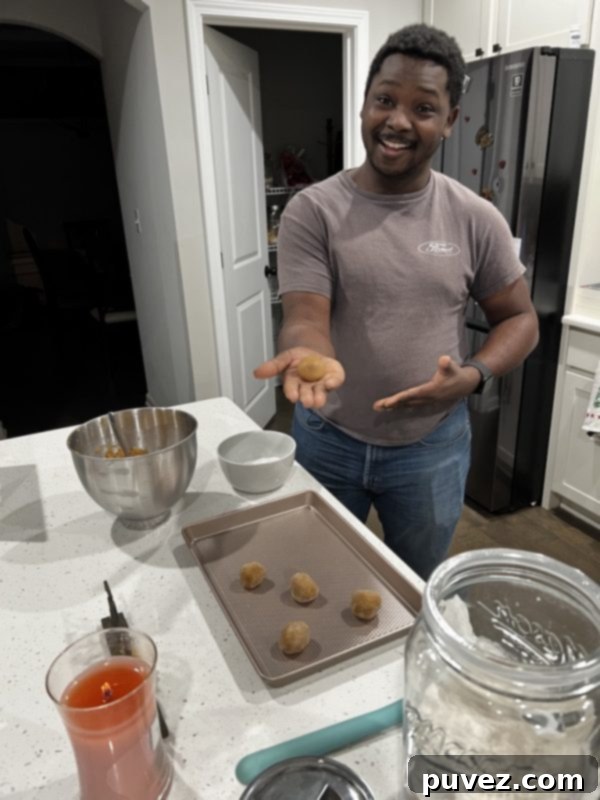 A hand rolling cookie butter dough into balls and placing them onto a baking sheet, coated in sugar