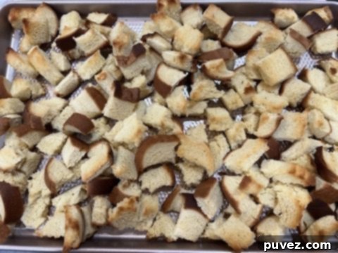 Lightly toasted brioche bread cubes spread on a cookie tray, ready for the casserole
