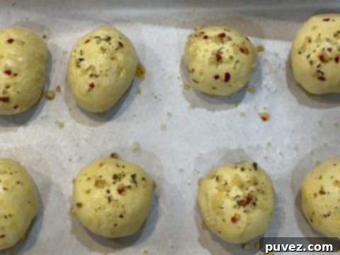 Cheesy Garlic Biscuit Bombs brushed with garlic butter on a baking sheet before baking.