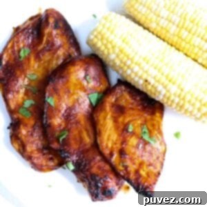 Three pieces of barbecue chicken with two ears of corn topped with pieces of cilantro and served on a white plate.