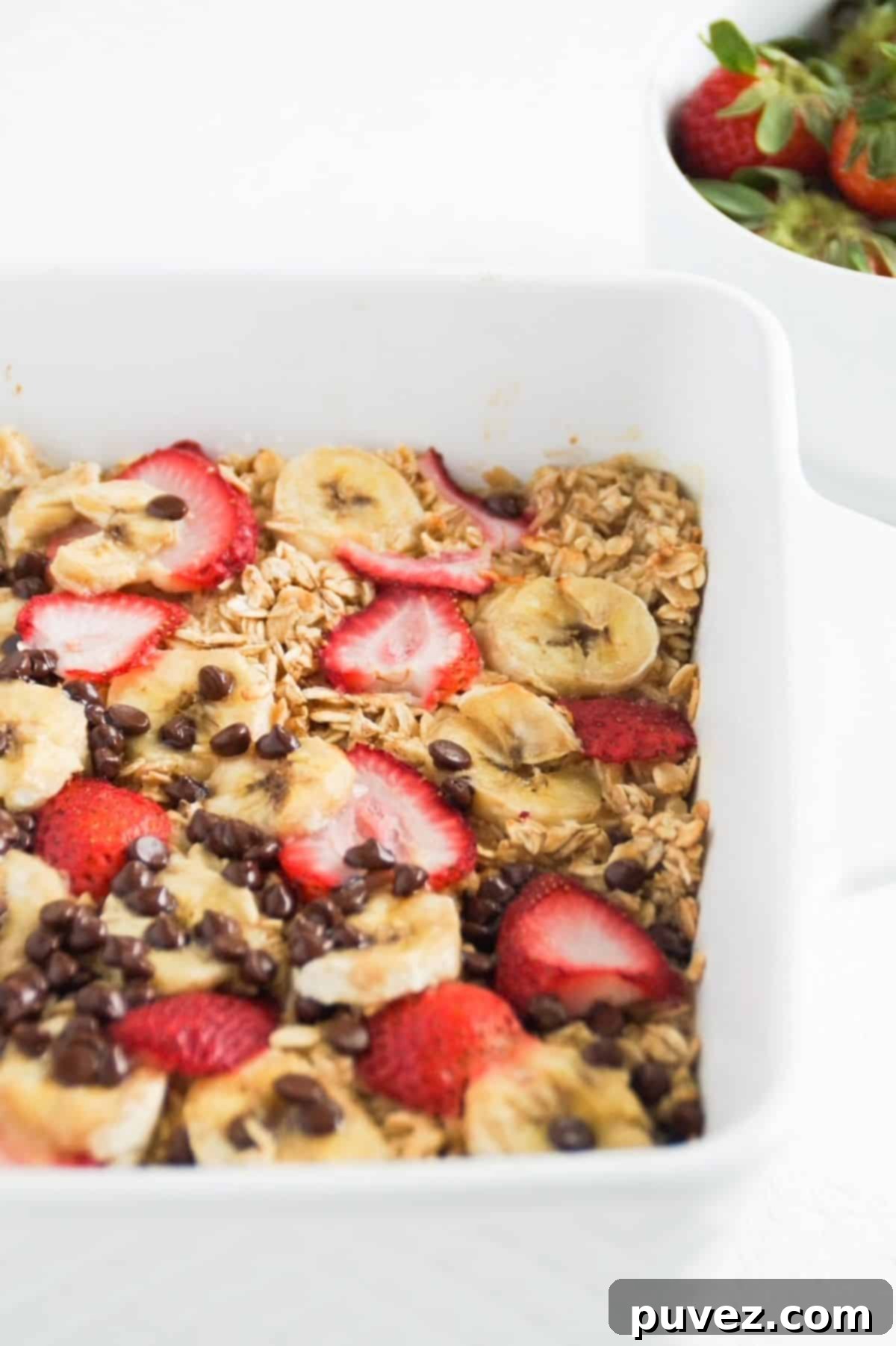 Banana baked oatmeal with strawberries and chocolate chips in a white dish.