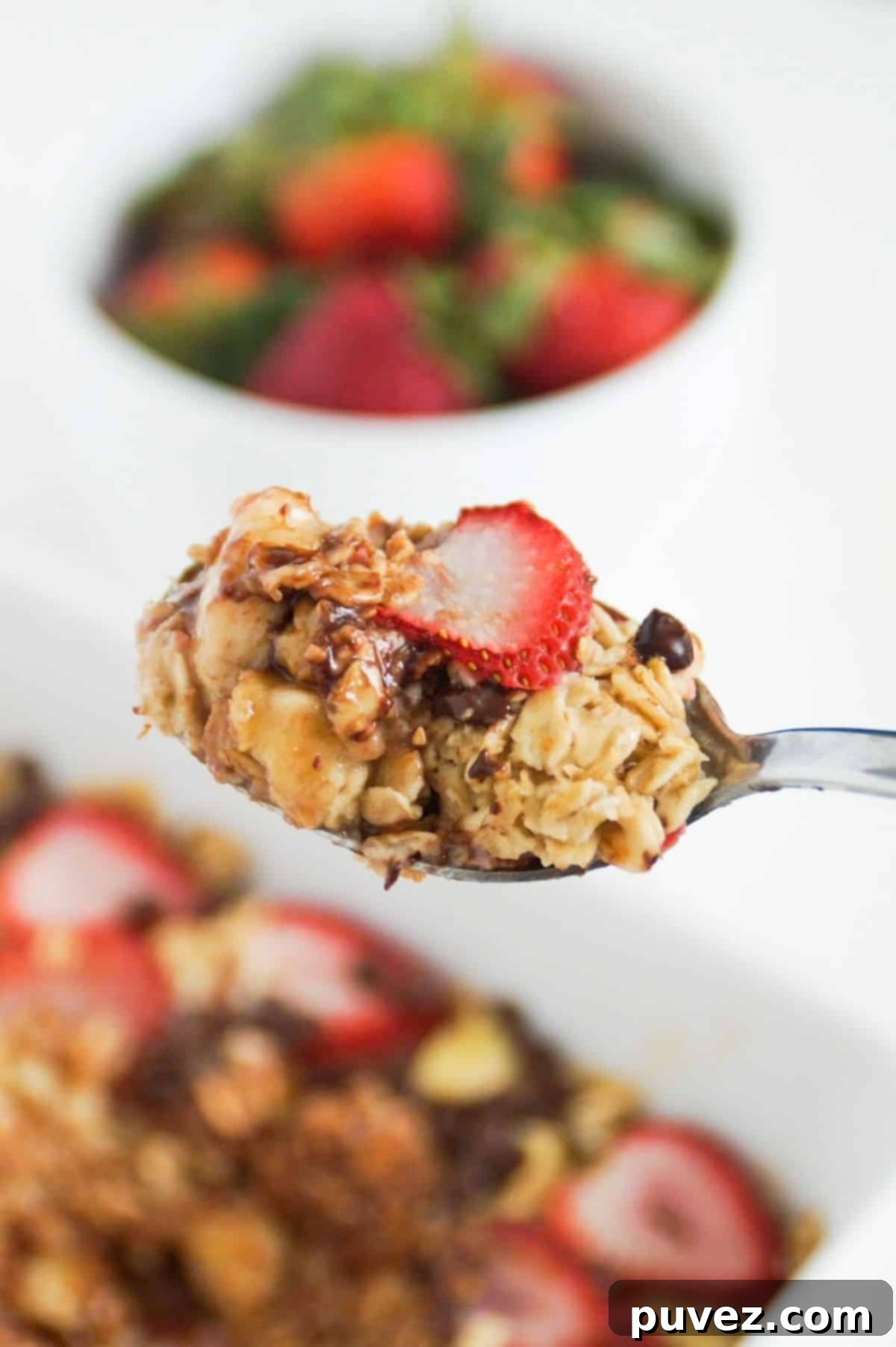 Banana and strawberry baked oatmeal on a spoon up close, with the rest in a serving dish in the background.