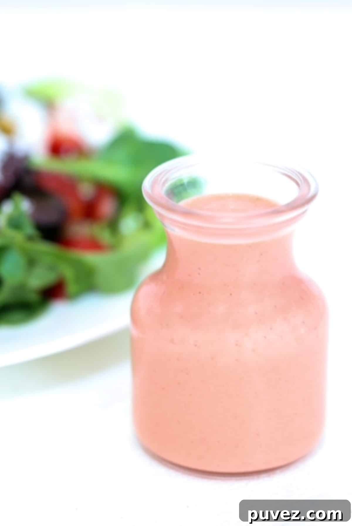 Strawberry Balsamic Salad Dressing in a glass dressing jar with a salad in the background.