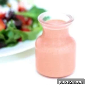 Strawberry balsamic vinaigrette in a glass jar with a salad in the background.