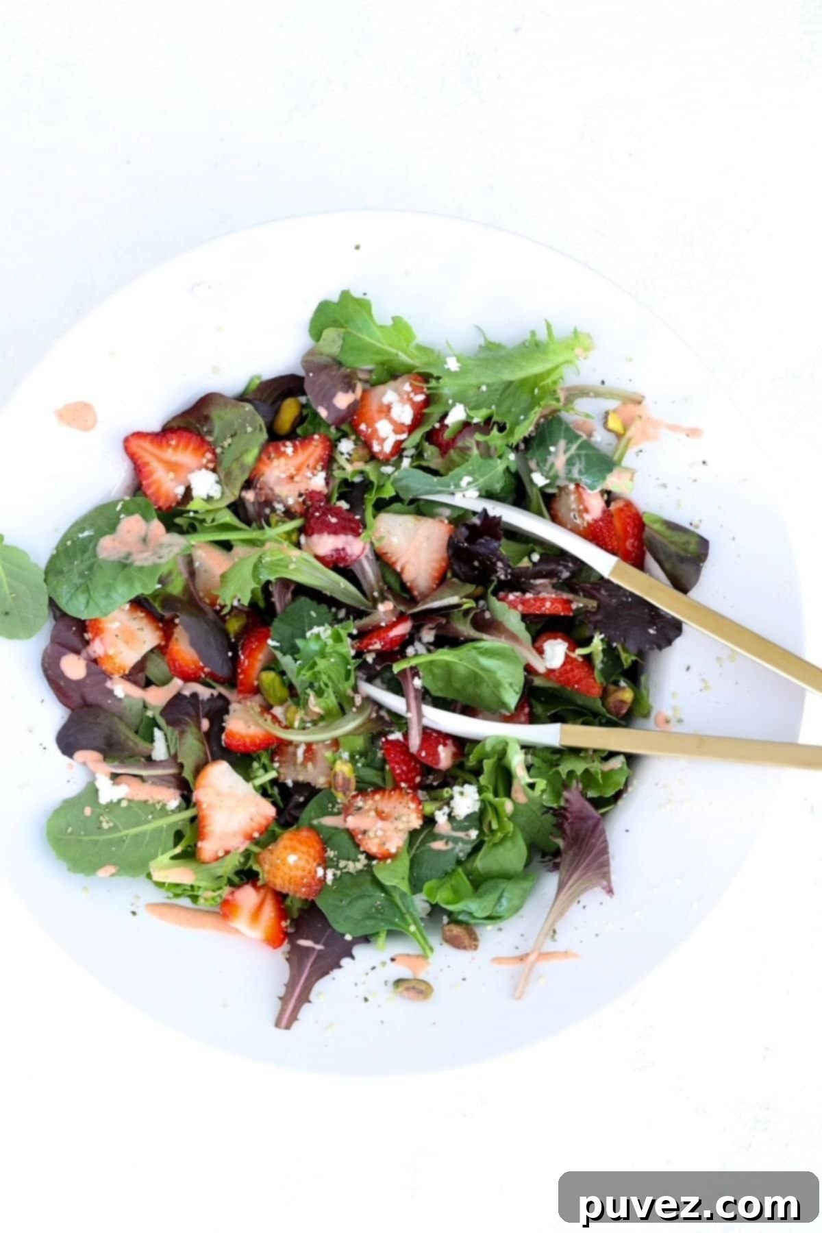Strawberry Goat Cheese Salad in a large white salad bowl with a pair of tongs.