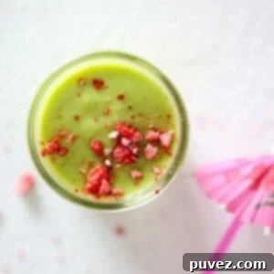 Island Green Paradise Smoothie 6 Top view of a vibrant green smoothie in a glass mason jar topped with crushed dried strawberry pieces, showcasing its refreshing appeal.