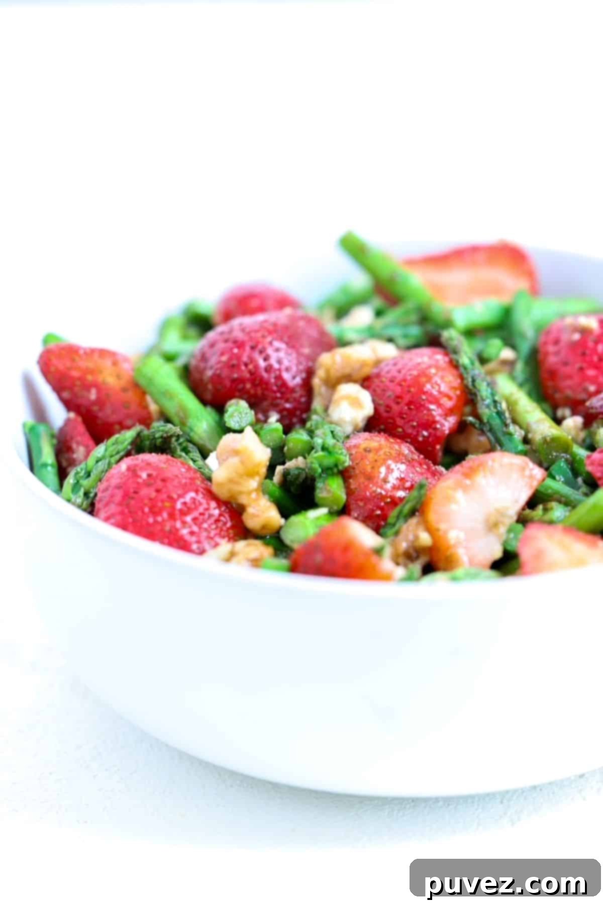 Simple Chilled Asparagus Salad 2 Cold asparagus salad with strawberries and feta in a white serving bowl, garnished with fresh herbs.