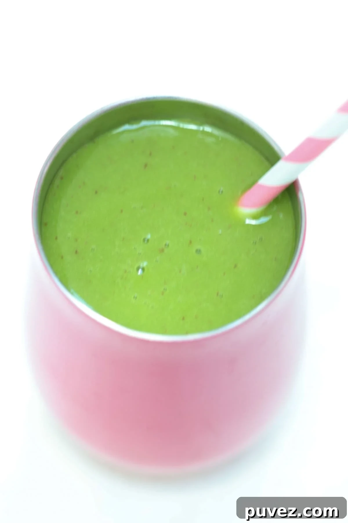 Top view of a mango spinach smoothie in a pink cup with a pink and white straw.