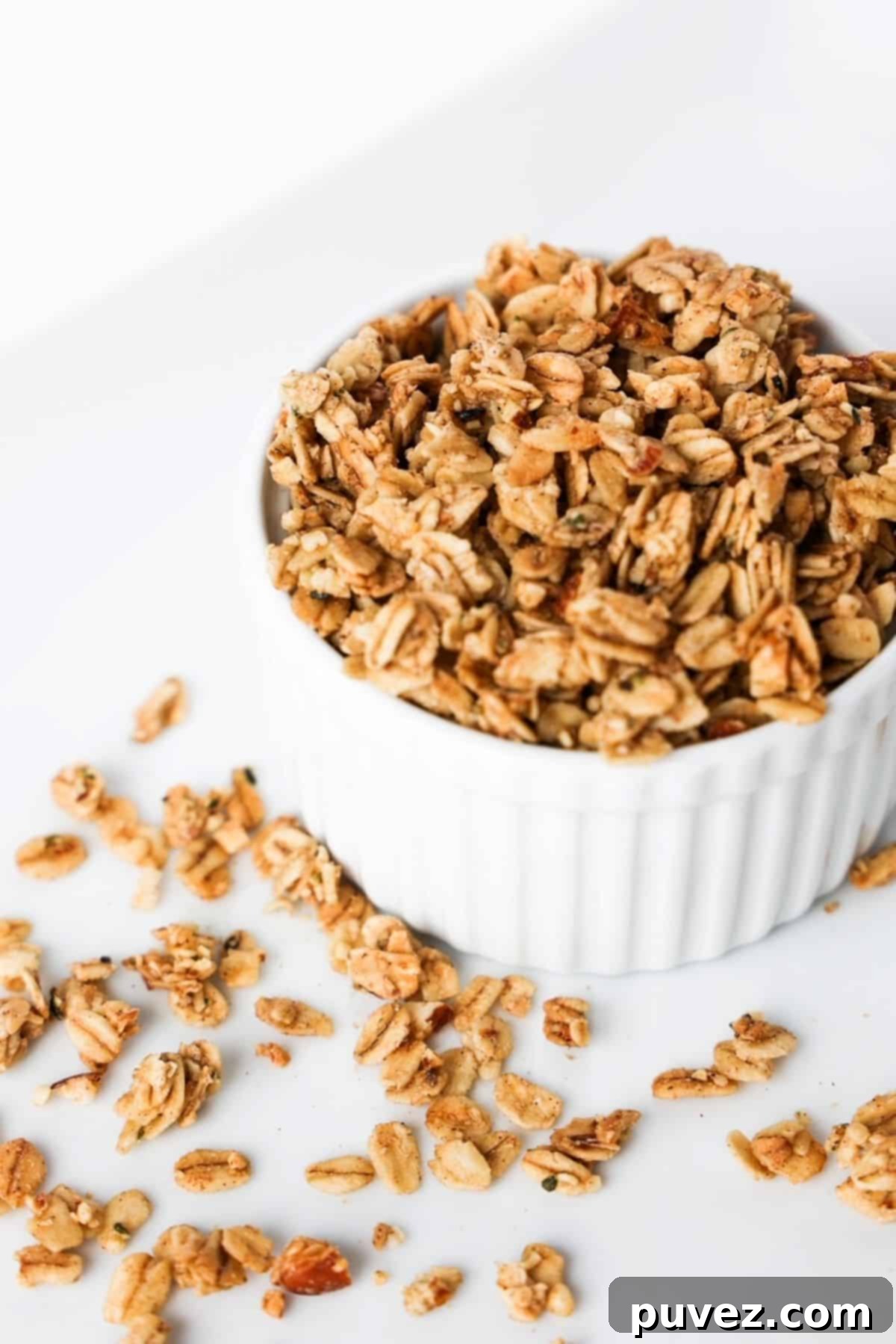 Granola in a white ramekin with pieces of granola scattered around the ramekin.