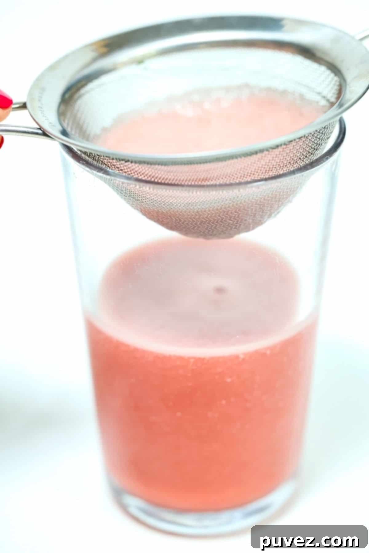 A small fine-meshed strainer sitting on the top of a glass of a watermelon smoothie.