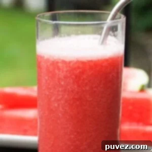 One tall glass of watermelon banana smoothie with a stainless-steel straw. A white plate with stacked watermelon slices is in the background.