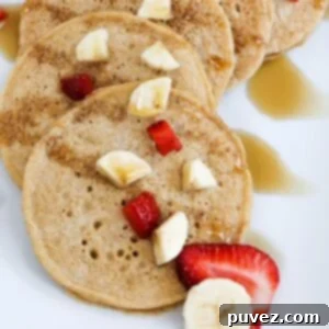 Pancakes overlapping each other, topped with pieces of strawberry and banana, and drizzled with maple syrup.