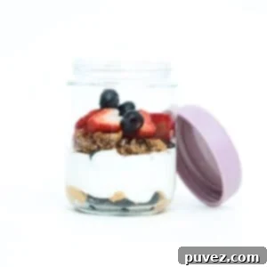 One Greek yogurt parfait with fresh berries in a glass jar with the lid off and leaning on the side of the jar.