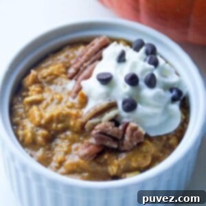 Top view of pumpkin overnight oats in a small white ramekin topped with pecans, whipped cream, and mini chocolate chips.
