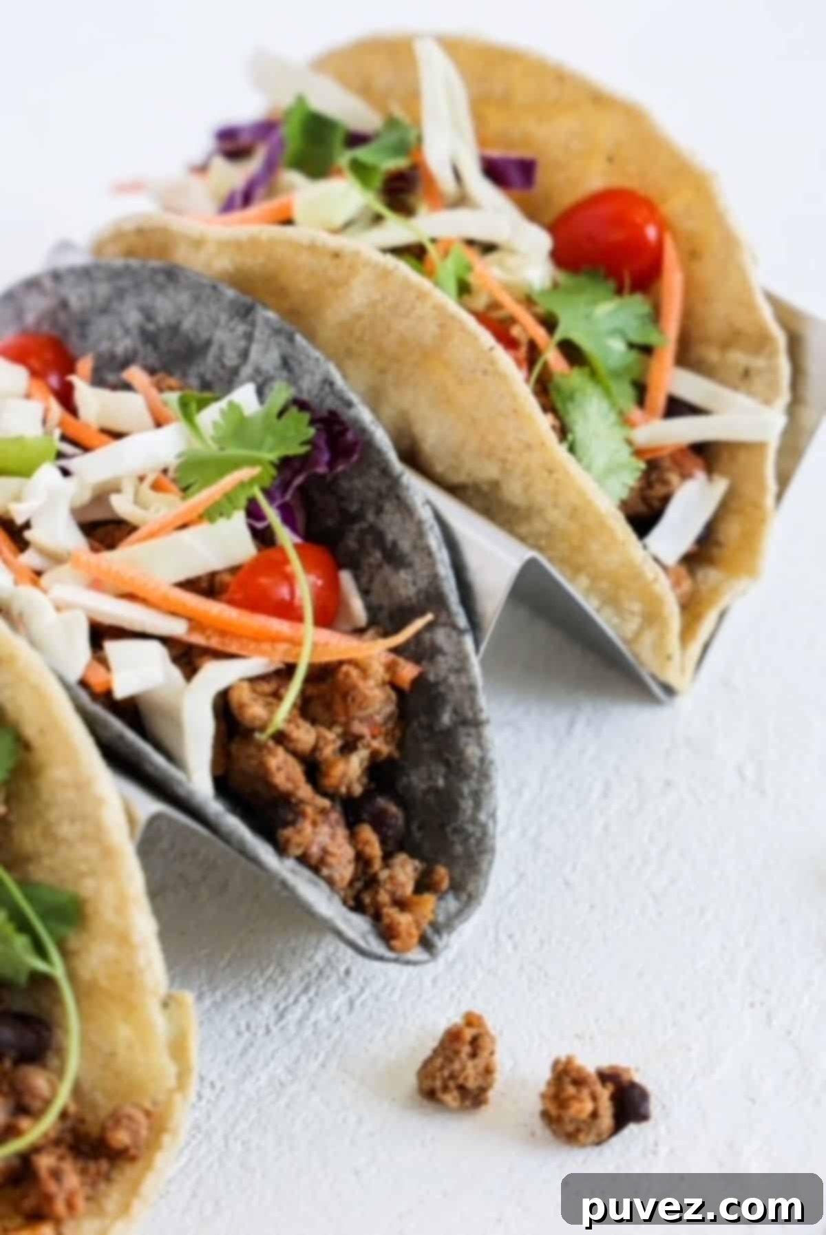 Three turkey tacos with toppings on a stainless steel taco holder. 