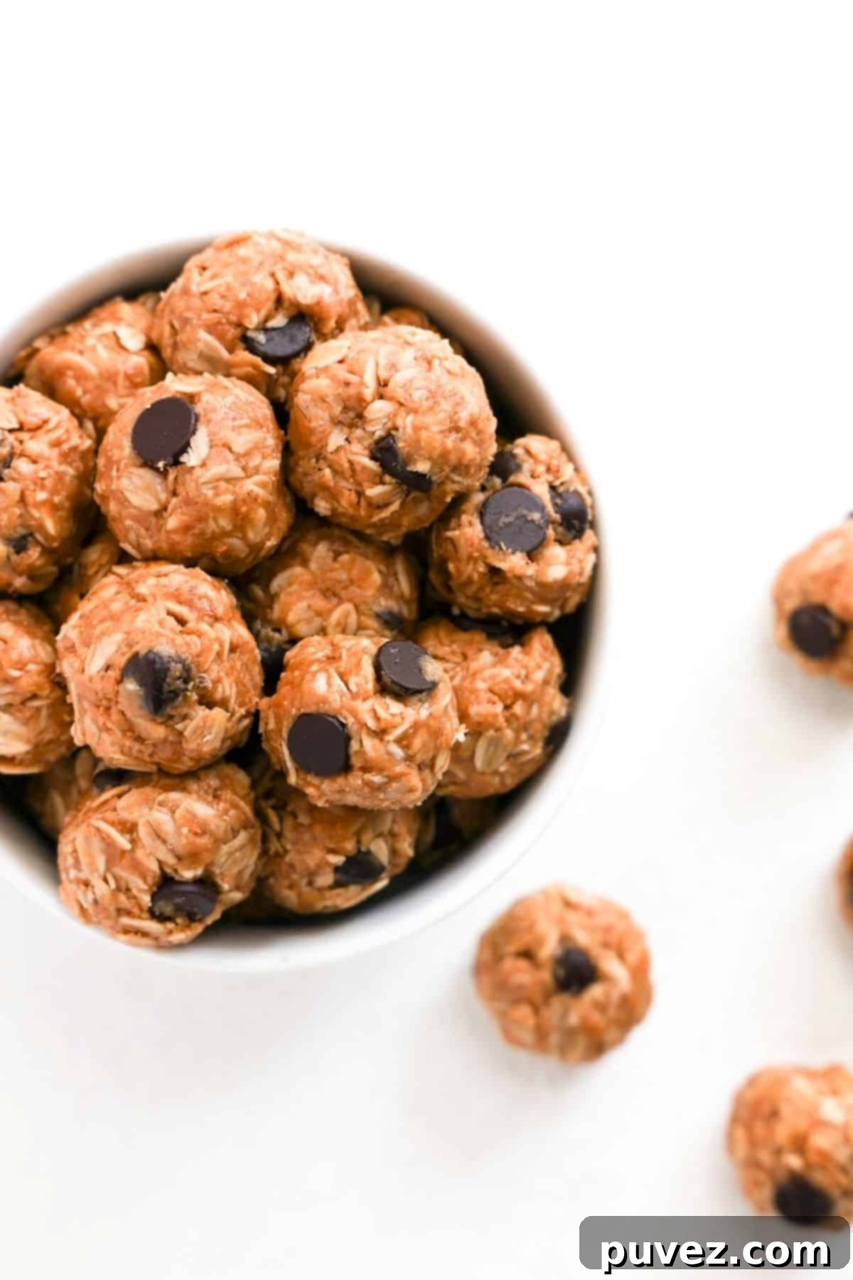 One white bowl filled with energy bites. A few energy bites are to the right of the bowl.