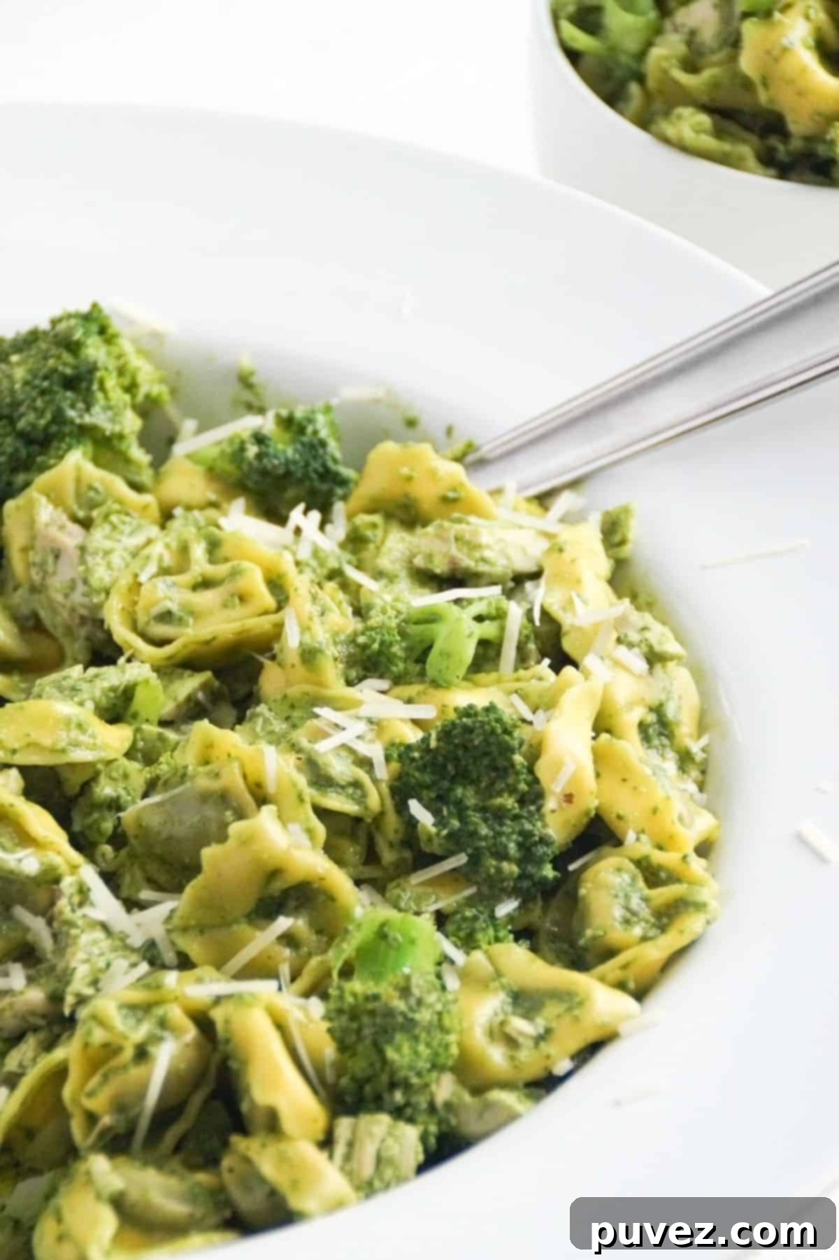Pesto with tortellini, chicken, and broccoli in a large white serving bowl with a spoon.