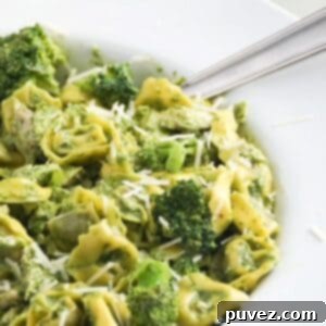 Pesto with tortellini, chicken, and broccoli in a large white serving bowl with a spoon.