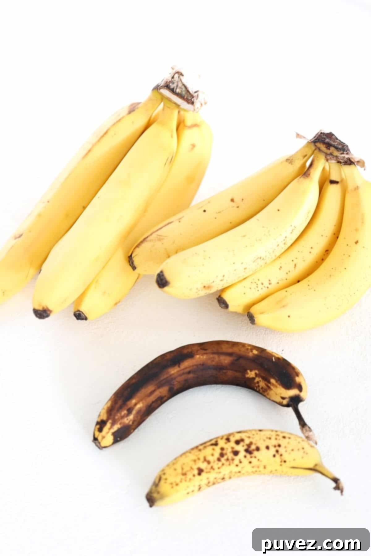 Two bunches of bananas and two individual bananas demonstrating different stages of ripeness, from green to heavily spotted brown.