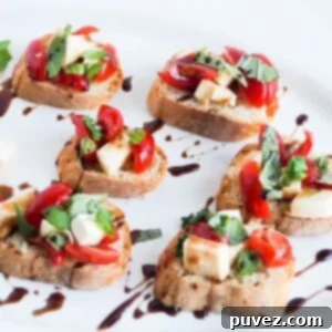 Six pieces of caprese bruschetta drizzled with balsamic glaze on a white platter.