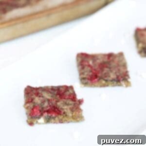 Two perfectly cut Raspberry and White Chocolate Blondies on a white serving platter, with a baking pan filled with more blondies visible in the background.