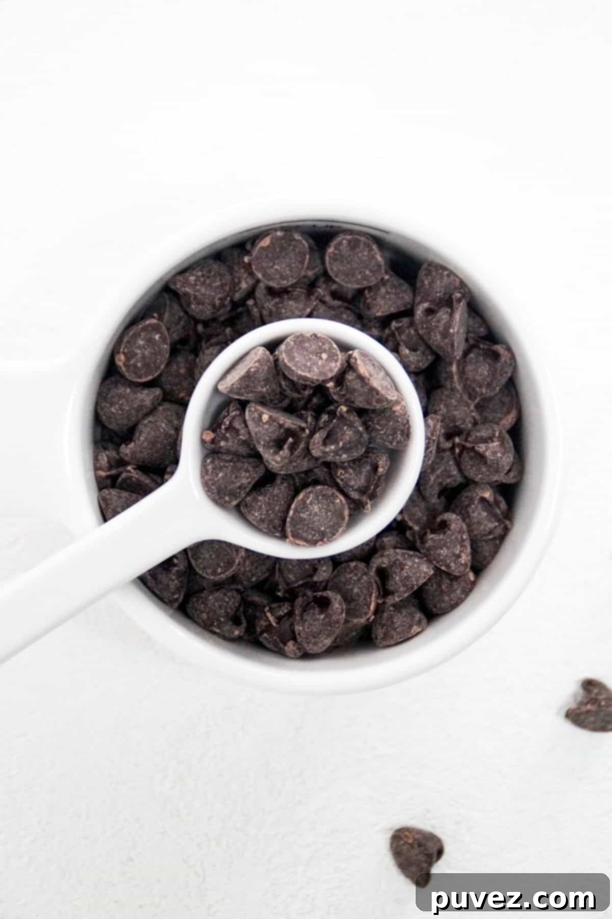 One tablespoon of chocolate chips held over a white measuring cup full of chocolate chips, illustrating the difference in volume.